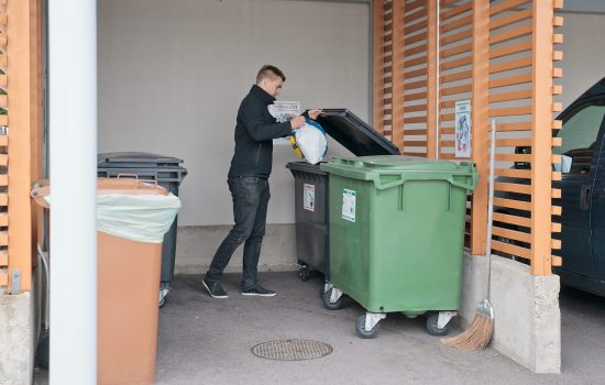 Mies viemässä roskia jätekatokseen